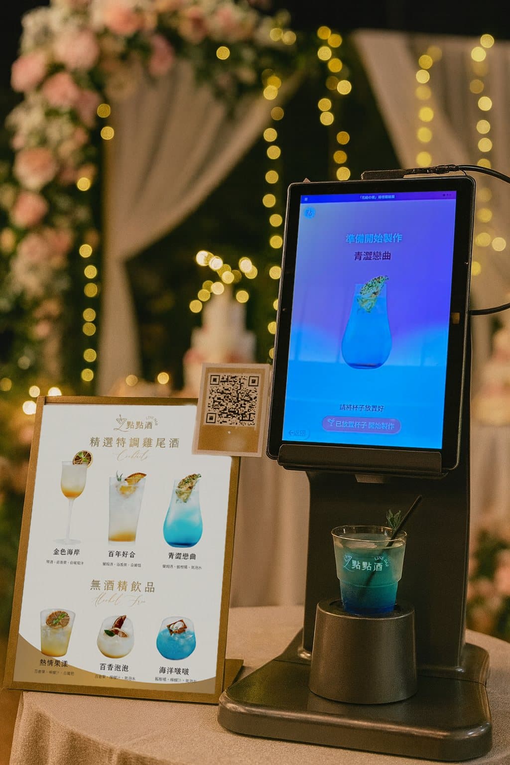 The wooden-housed smart bar with a lit dispensing aperture, a screen showing bottle artwork and florals on top