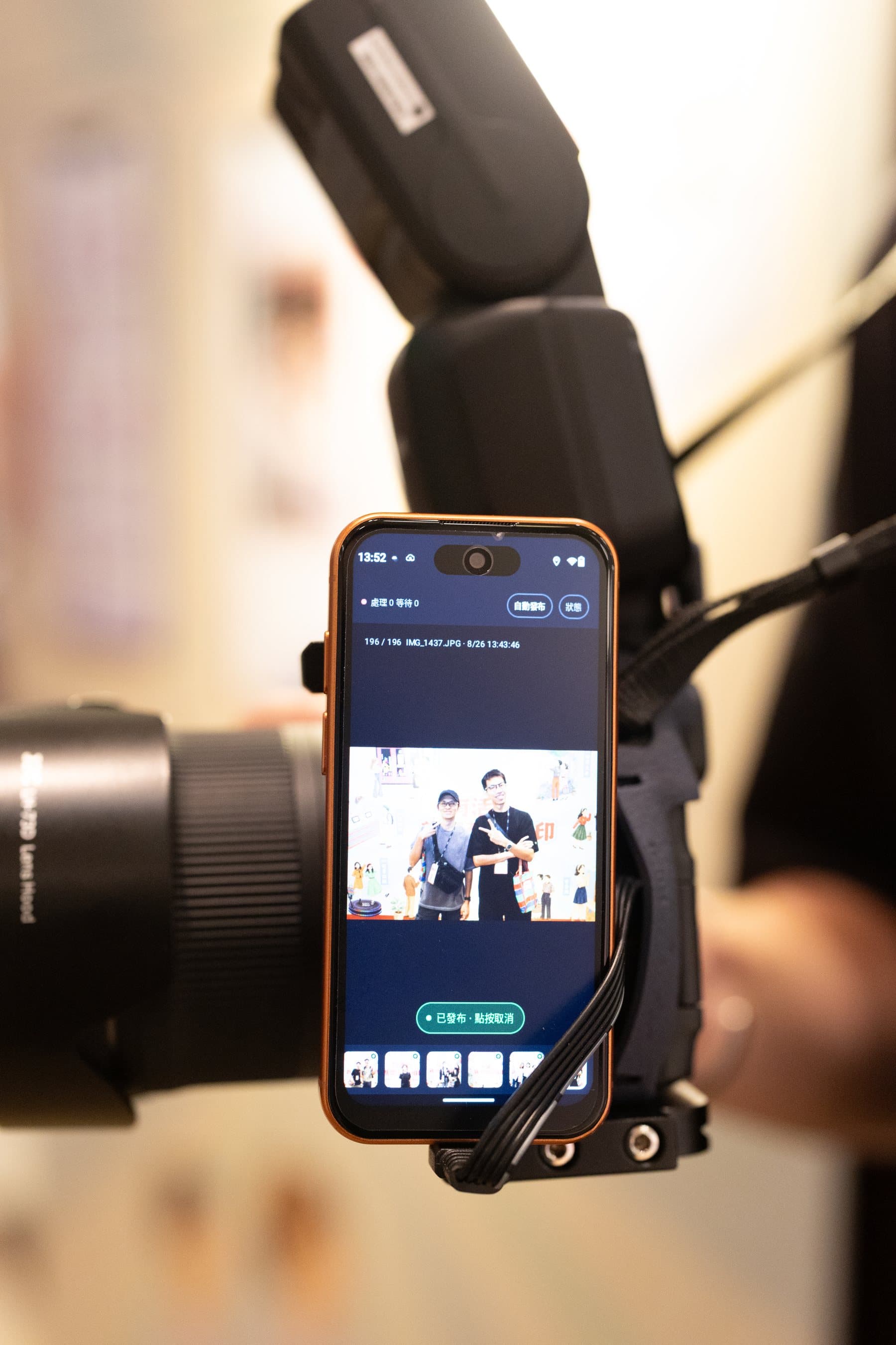 The phone mounted on the photographer’s camera, its screen showing the shot just taken with the upload queue at zero and auto-publish on