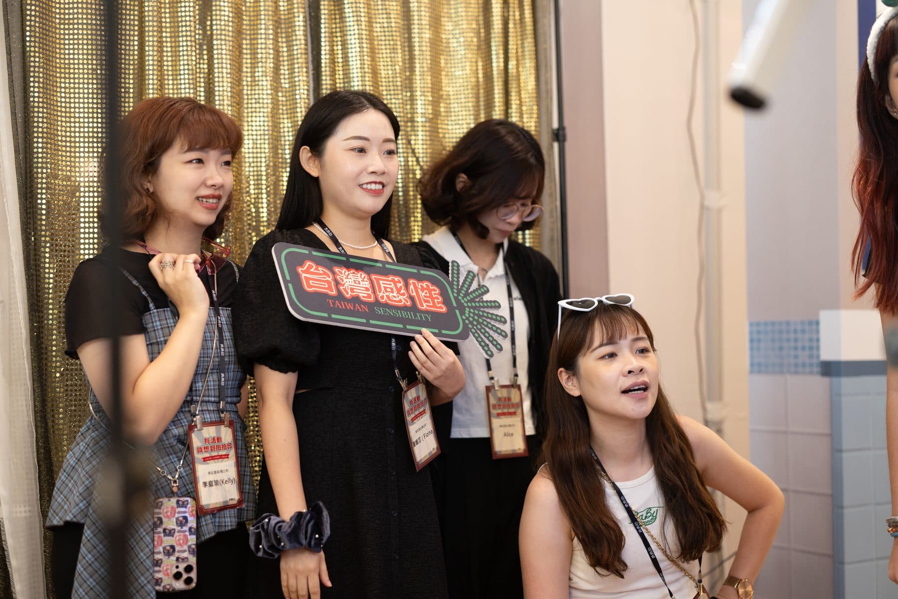 Four guests posing at a gold sequin backdrop with a neon-style Taiwan prop sign