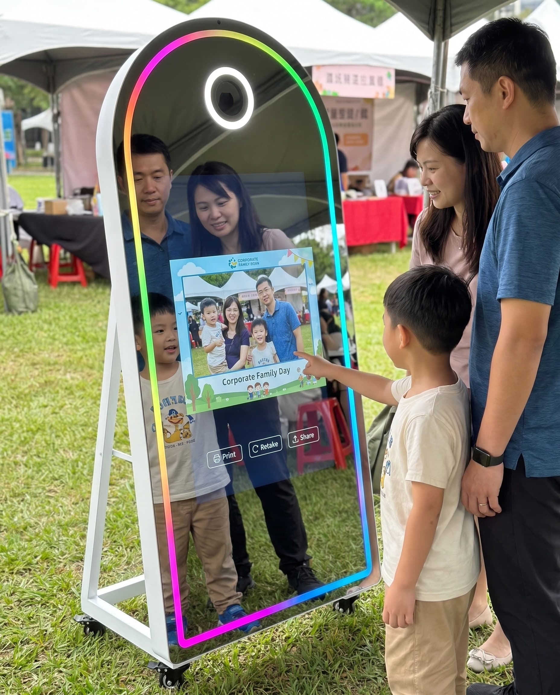 A family at the magic mirror at an outdoor family day, kids making faces