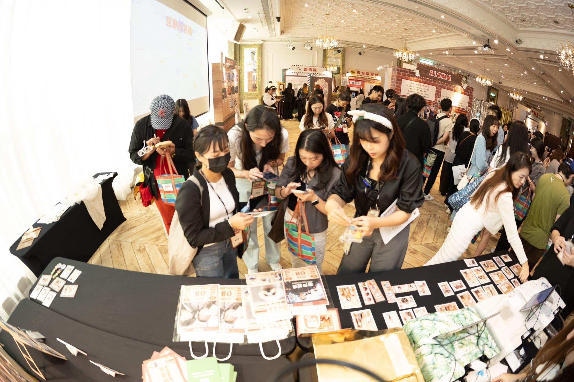 A row of guests around the collection table, prints spread across it, most of them holding phones