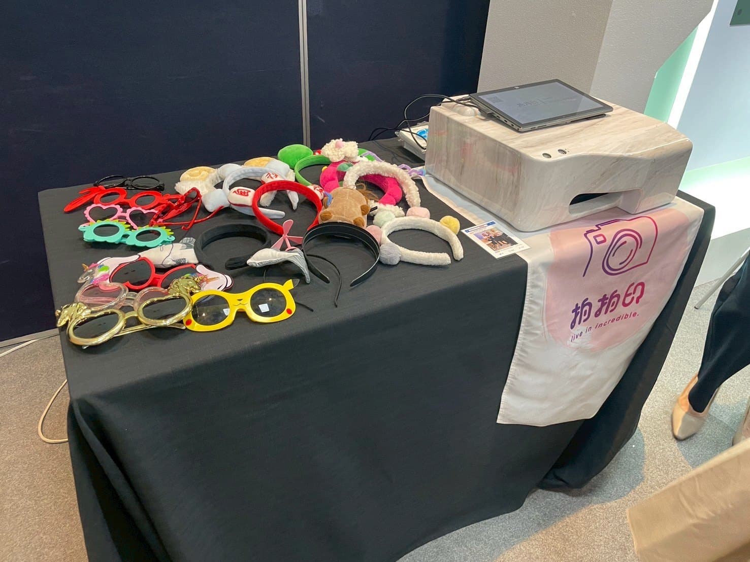 A draped table holding two photo printers, a tablet and a tray of headbands and prop glasses